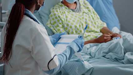 Fototapeta premium Close up of specialist holding checkup documents to cure patient with sickness in hospital ward. Doctor using medical files to do healthcare consultation while wearing face masks.