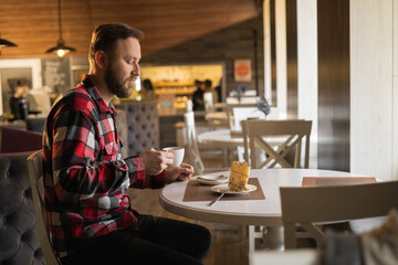 Fototapeta na wymiar side view of young man having cup of coffee and eating pastry in a cafe