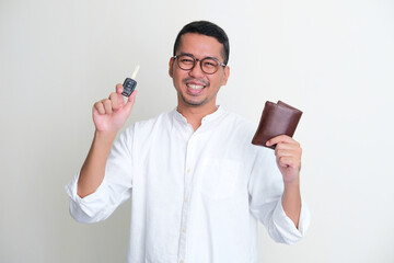 Adult Asian man smiling confident while showing his wallet and car key - obrazy, fototapety, plakaty