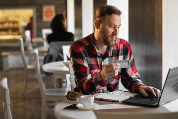 Fototapeta premium handsome businessman shopping online with credit card using laptop in cafe, young man sitting in cafe while using laptop computer and debit card.
