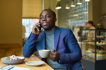 African young businessman having a conversation on mobile phone during coffee break at coffee shop