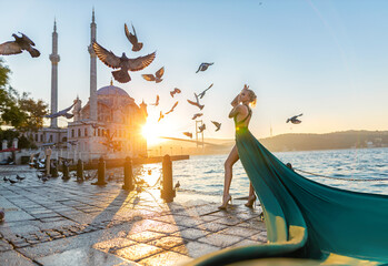 Woman in long green dress posing with flying pigeons at the historical square near Ortaköy mosque...