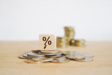 decreasing percent sign on wooden cube block on pile of coins and blurred stack of coins