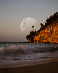 Looking out to the ocean with a super moon behind a rocky cliff 