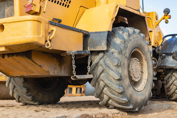 Fototapeta na wymiar Big rubber wheels of soil grade tractor car earthmoving at road construction side. Close-up of a dirty loader wheel with a large tread against the sky.