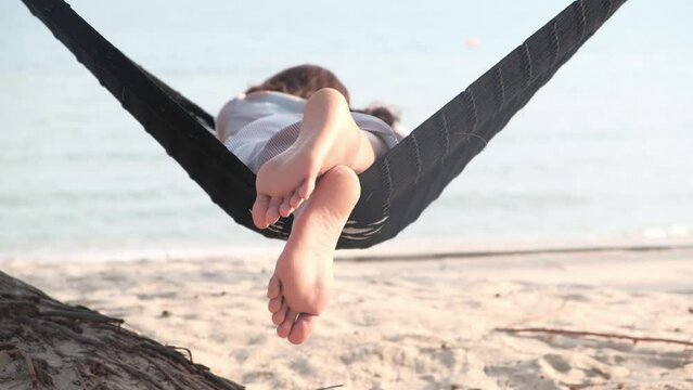 Feet of a beautiful woman. She lies in a hammock on the beach of the sea. In the summer she feels the good weather. she is on vacation