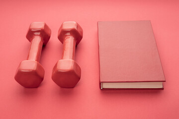 two red dumbbells on a red background, next to a red book