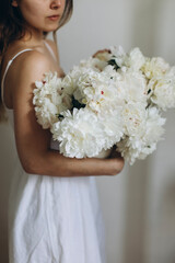 bouquet of white peonies in the hands of a young woman in a white dress. young beautiful woman in a white dress holding a bouquet of white flowers