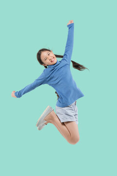 Happy little Asian child girl jumping isolated on pastel green background.