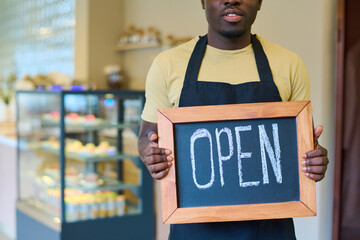 Close-up of african male owner holding blackboard with open sign in his hands, he opening his new coffee shop