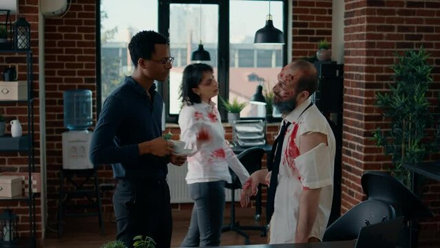 Businessman in office workspace discussing with creepy zombie work colleague. Scary undead person covered in blood and with grunge evil look getting closer to man while acting bizarre and spooky.