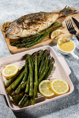 dorado fried on a wooden board next to asparagus sauce and a black fork with a knife