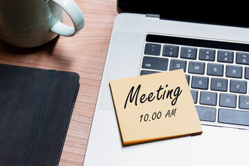 Top view memo paper with message meeting 10.00 AM on laptop