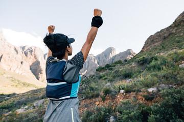 Woman standing in valley looking at mountain with raised hands
