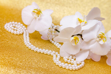 white Orchid and pearl necklace on a shiny gold background
