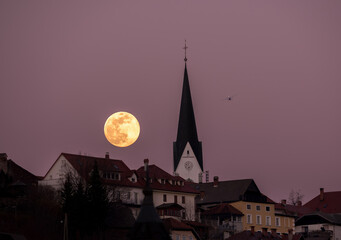 Full moon rising behind the city with mountains in the background.  - obrazy, fototapety, plakaty
