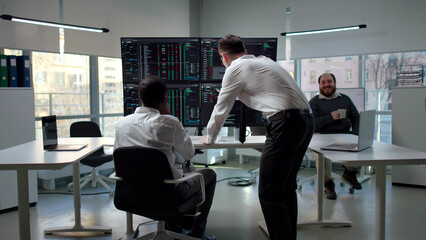 Back view of professional traders analyzing stock market exchange graphs pointing at monitor 