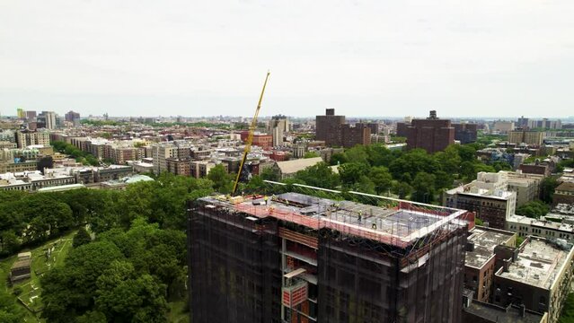 New residential development in Harlem, NYC. 360 drone shot of Manhattan with crane and construction crews at work.