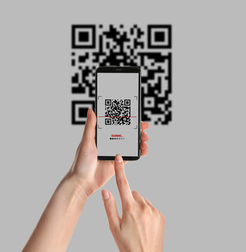 Woman scanning QR code with smartphone on light background, closeup