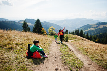 Woman is traveling with a childrens. Mom in the mountains. Climb to the top of the mountain with children. With the backpack climbed to the top.