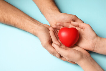 Couple holding red heart in hands on light blue background, closeup