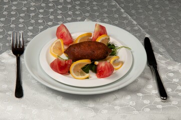One kibbeh, lemon and tomato in a white ceramic plate. Kibbeh, a dish unique to the Middle East cuisine, is made with bulgur, ground beef, onion and tomato paste.