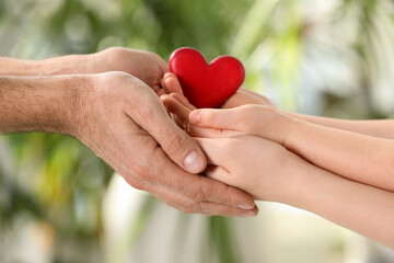 Fototapeta na wymiar Parents and kid holding red heart in hands on blurred green background, closeup