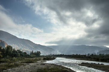 A river among the mountains with colorful autumn foliage and a bright sky.