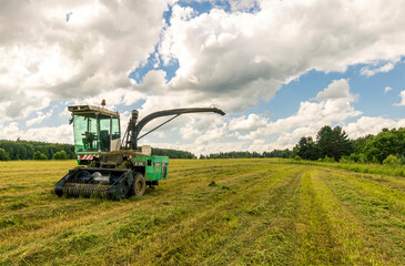 combine harvester gathering harvest on a agricultural field with cloudy sky and green forest on thr...