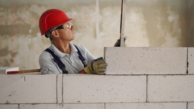 Bricklayer using spirit bubble and laser level to precise check concrete blocks on wall. Contractor uses tools for brickwork. Worker constructs a wall in new apartment real estate.