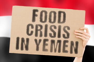 The phrase " Food crisis in Yemen " is on a banner in men's hands with a blurred Yemeni flag in the background. Crisis. Finance. Life. Nutrition. Bread. Disaster. Collapse. Social issue. Problem