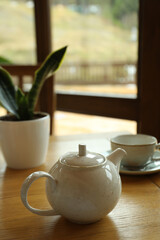 Teapot, cup and plant on wooden table in restaurant