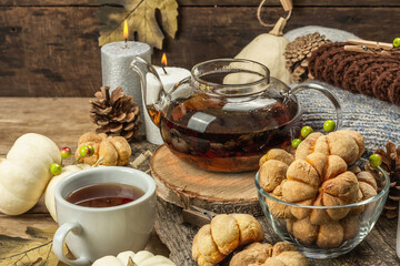 Autumn tea concept. Cookies with pumpkin puree, black tea in a glass teapot, fall decor