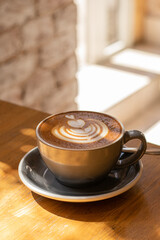 Cup of cappuccino on the wooden table in cafe. Sunny day, hard light. Сoffee foam, latte art