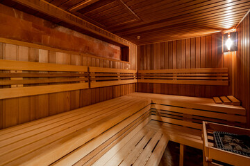 Fototapeta na wymiar Seat in sauna room. Empty wooden steam room with stone heater.Sauna room for good health. Sauna room with traditional sauna accessories.Healthy and spa life style. 