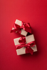 Two gift boxes tied red ribbons on red background.