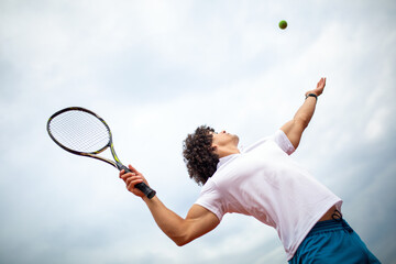 Young handsome tennis player with racket and ball prepares to serve at beginning of game or match.