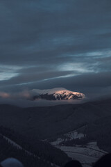 Sunlight breaks through the rain clouds and gently falls on the top of a snow-capped mountain.