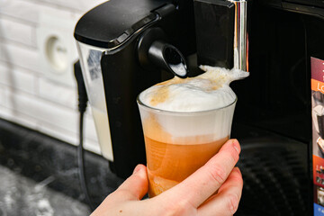 The girl puts a glass cup into the coffee machine to make coffee.