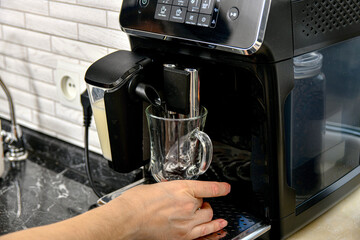 The girl puts a glass cup into the coffee machine to make coffee.