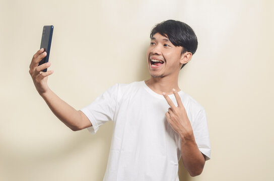 asian man wearing white t-shirt with gesture taking photo using smartphone on isolated background