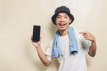 asian man wearing bright white t-shirt in black hat with blue towel pointing at phone screen on isolated background