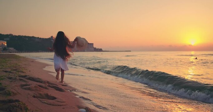 Beautiful ocean beach sunrise and happy running girl on the seashore, footprints in sands
