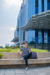 Young caucasian man in casual clothing sitting near modern office building and making video call. High quality photo