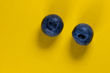 Two blueberries on a yellow background