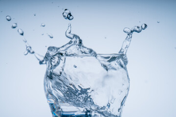 Ice cube fell into the glass of water. Water splashed from the clear glass. Fresh concept
