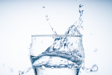 Ice cube fell into the glass of water. Water splashed from the clear glass. Fresh concept