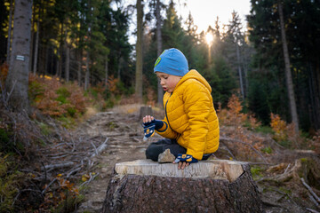 Fototapeta na wymiar Little kid is sitting on a big stump on the mountain trail, eating. Fall season