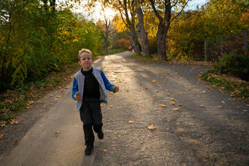 Fototapeta premium The little kid is running along the asphalt road after the hike is over. Fall season