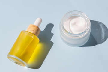 Facial serum dropper and moisturizer cream in glass bottle and jar on blue background. Eco organic natural beauty skincare products, top view. mockup for cosmetic brand